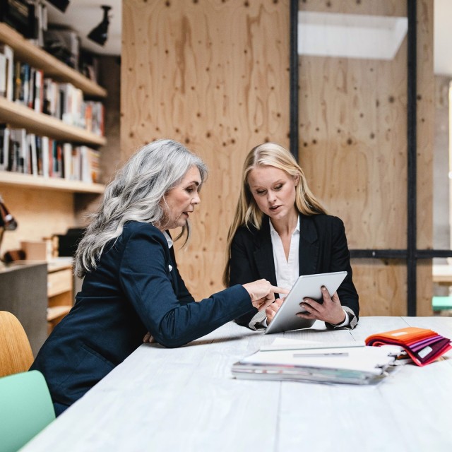 Zwei Frauen sitzen an einem Tisch und arbeiten mit einem Tablet