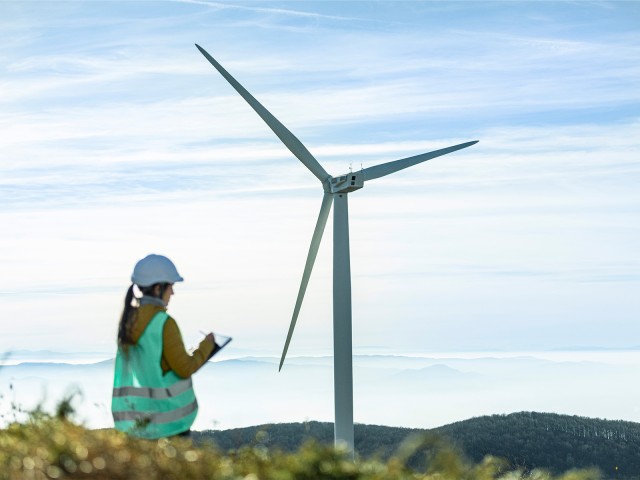 Frau in Warnweste vor einem Windkraftanlage