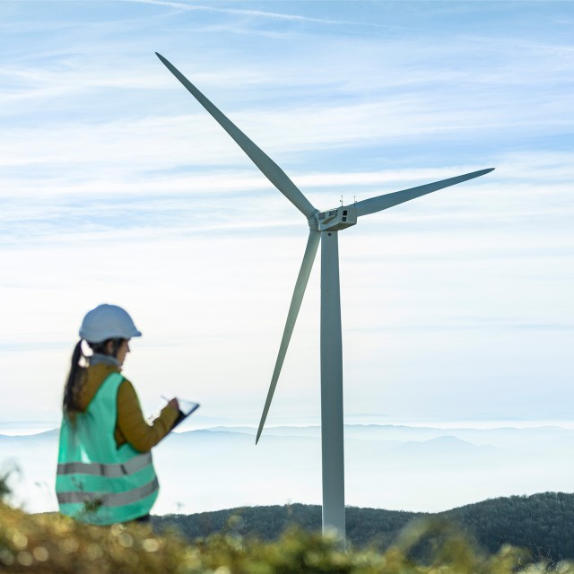 Frau in Warnweste vor einem Windkraftanlage