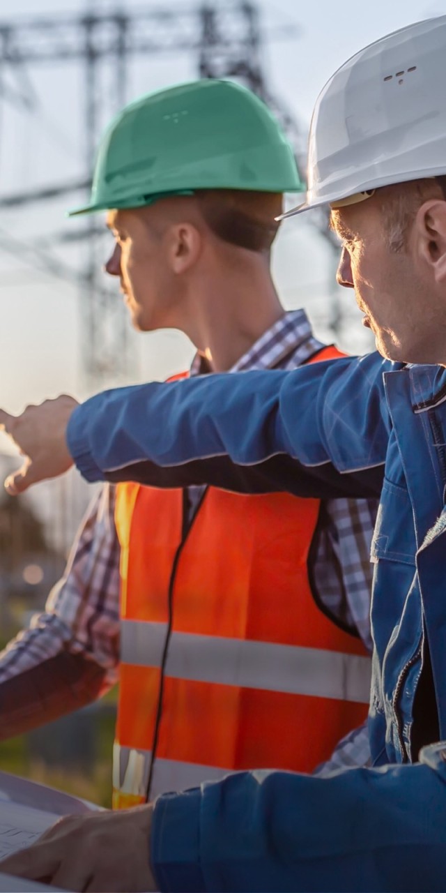 Bauarbeiter stehen vor Strommasten im Sonnenuntergang