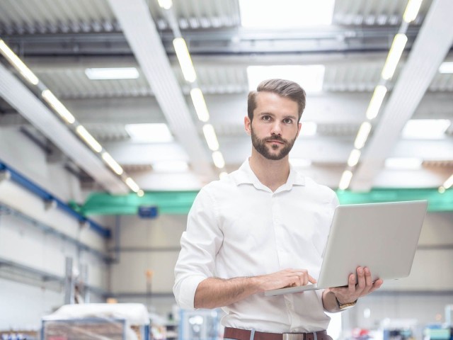 Mann hält Laptop in einer Fabrikhalle 