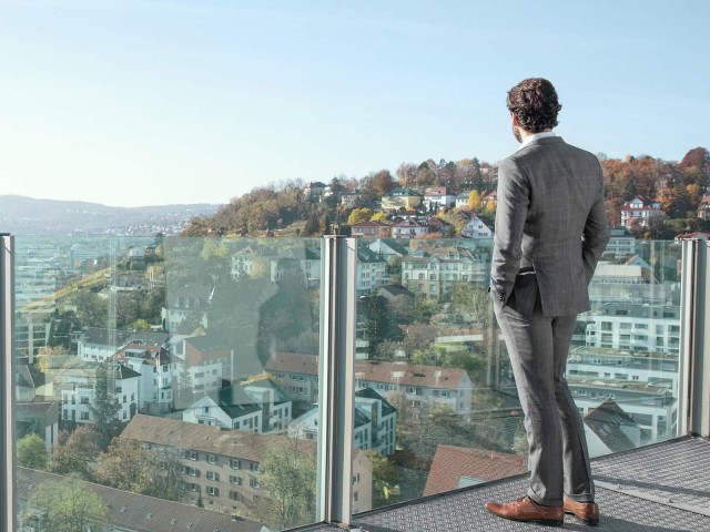 Man looks at a city from a glass balcony 