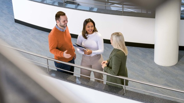 Drei Personen unterhalten sich im Flur eines Bürogebäudes.