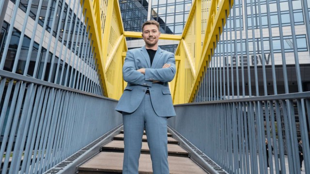 Ein Mann steht mit verschränkten Armen auf einer Brücke mit gelbem Geländer.