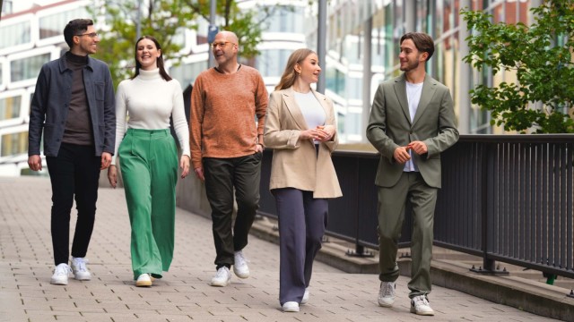 Fünf Personen gehen auf einem Bürgersteig und unterhalten sich.