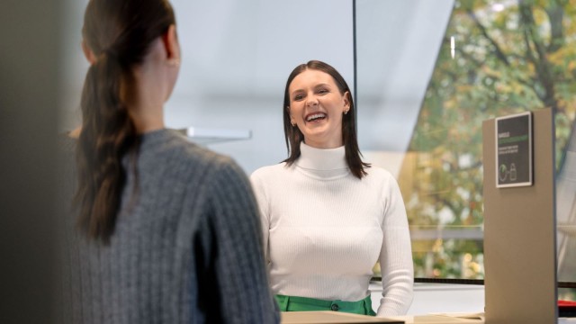 Eine junge Frau lächelt eine Person am Schalter an.