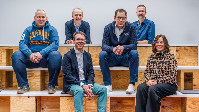 Sechs Personen sitzen auf Holzkisten.