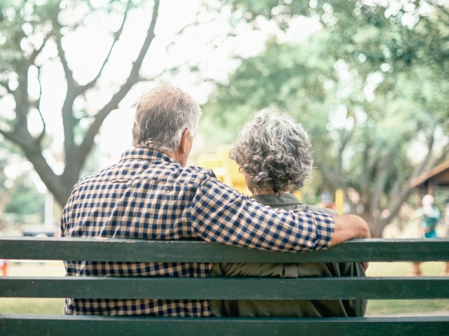 Älteres Ehepaar sitzt auf Bank und blickt in die Weite