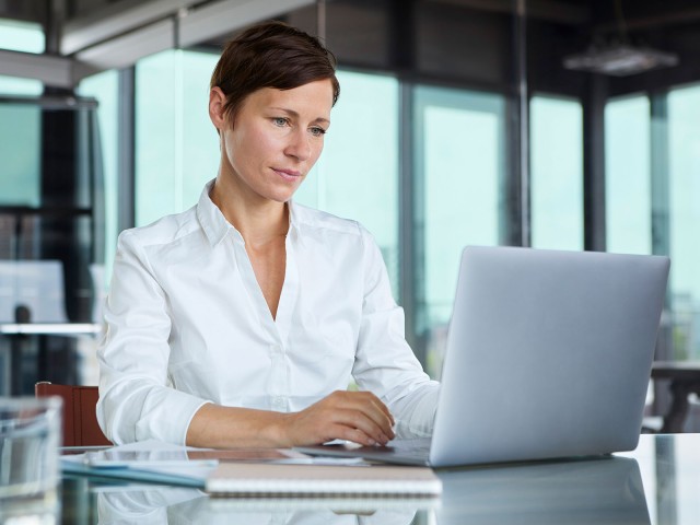 Geschäftsfrau sitzt in vergöastem Konferenzraum am Laptop