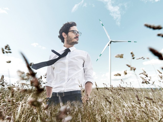 Mann mit Brille und Krawatte steht im Feld vor Windrädern