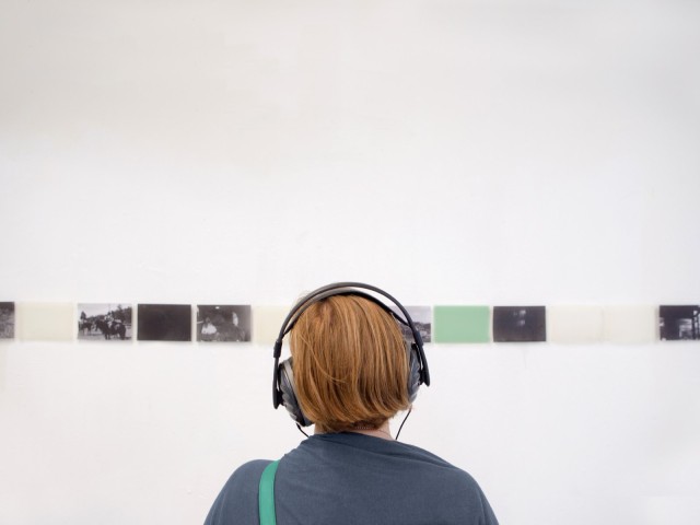 Frau mit Kopfhörern schaut Kunstwerke an Wand an