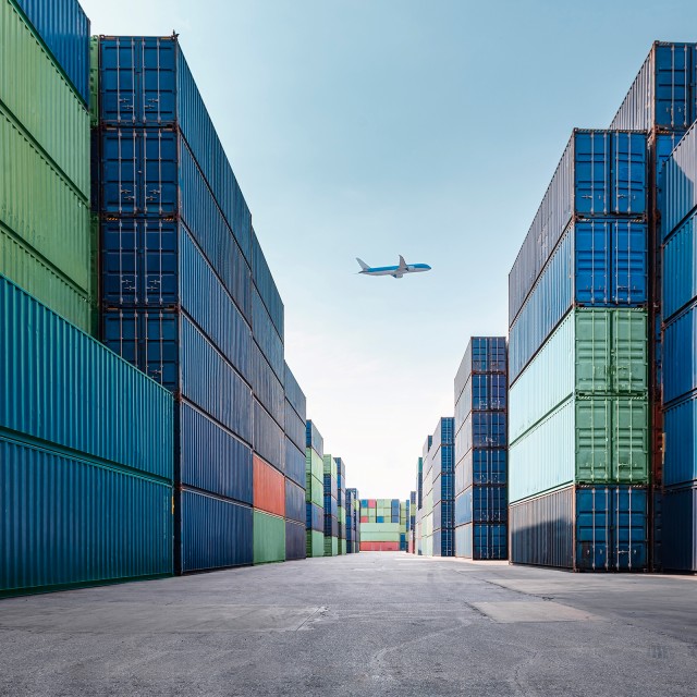 An airplane flies over freight containers