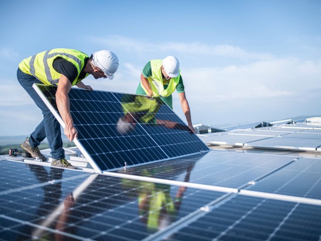 Zwei Ingenieure installieren Sonnenkollektoren auf einem Dach