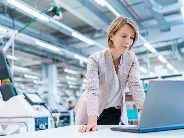 Geschäftsfrau steht in moderner Fabrikhalle am Laptop